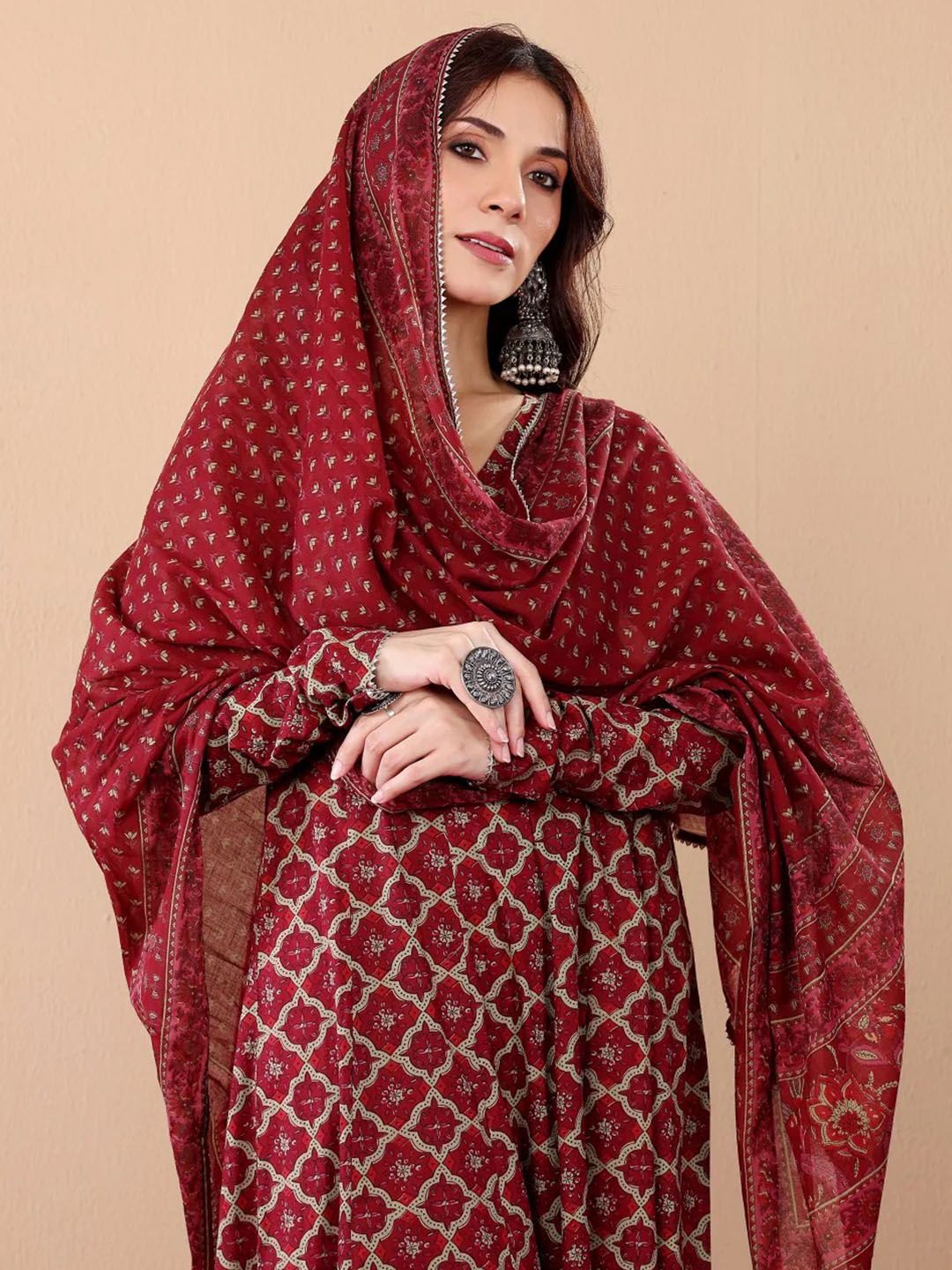Woman wearing a red patterned outfit with a matching shawl against a beige background