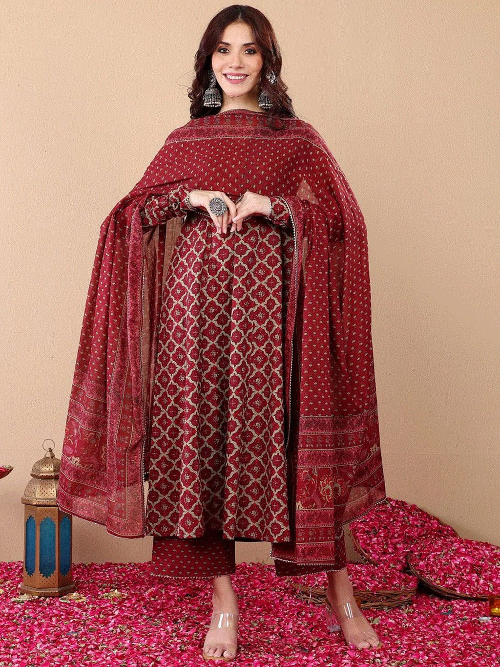 Woman wearing a red patterned outfit with a matching dupatta on a beige background