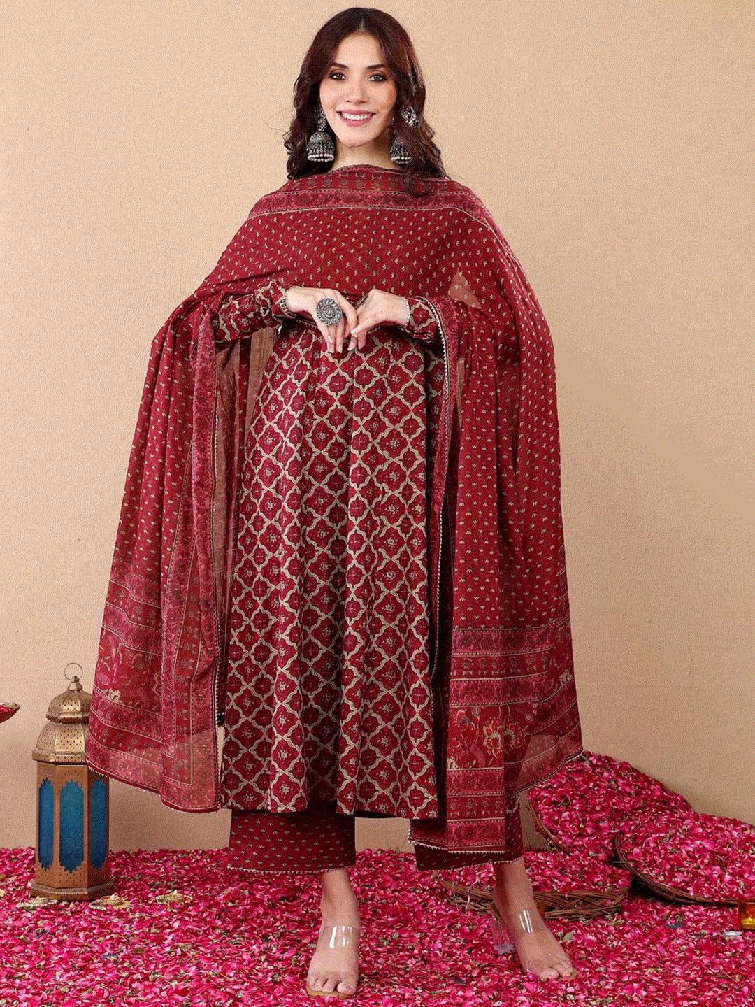 Woman wearing a red patterned outfit with a matching dupatta on a beige background