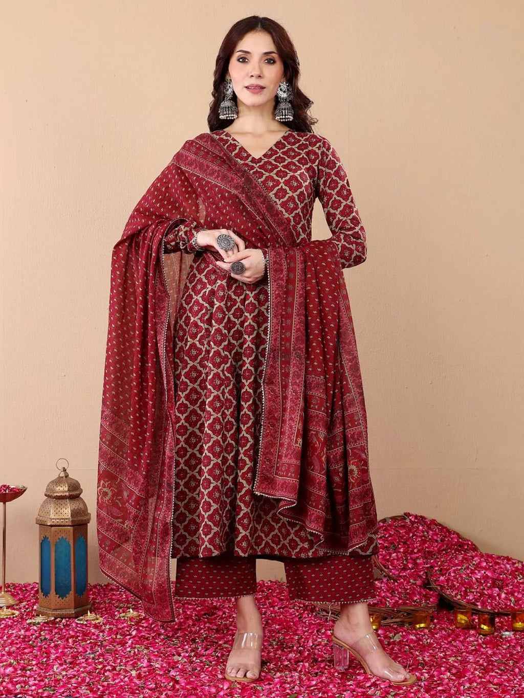 Woman wearing a red patterned traditional outfit with a dupatta on a beige background