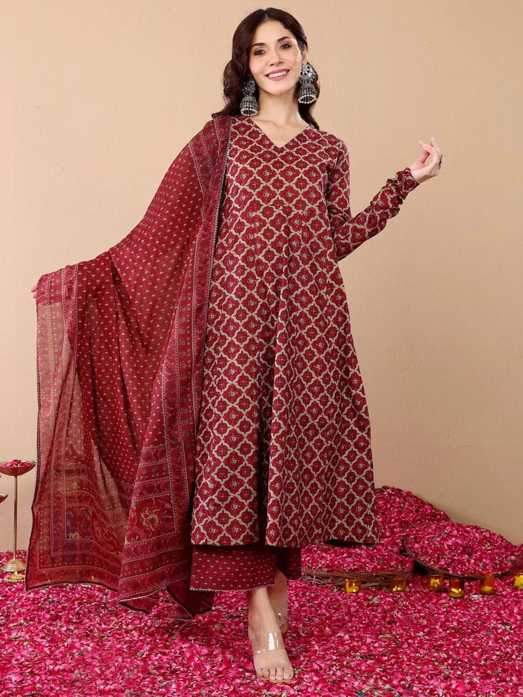 Woman wearing a red patterned outfit with a matching dupatta on a beige background