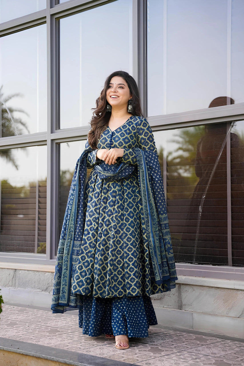 Woman in a blue patterned traditional outfit standing outside a building with large windows.