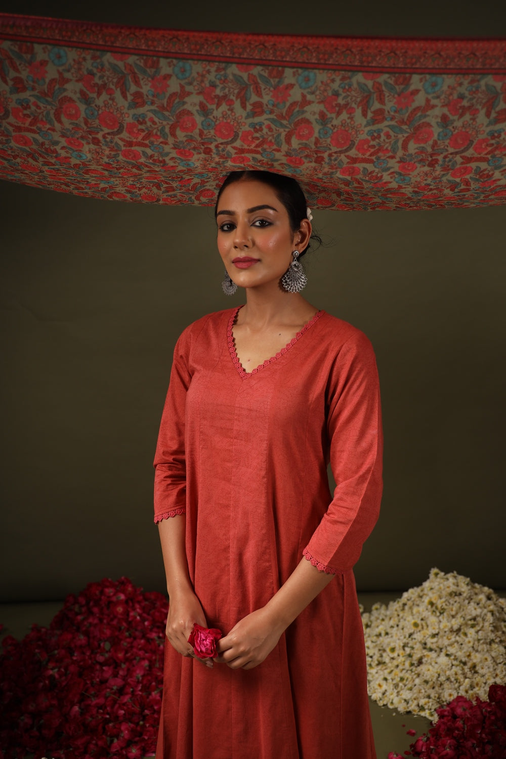 Woman in a red dress holding a flower against a decorative background