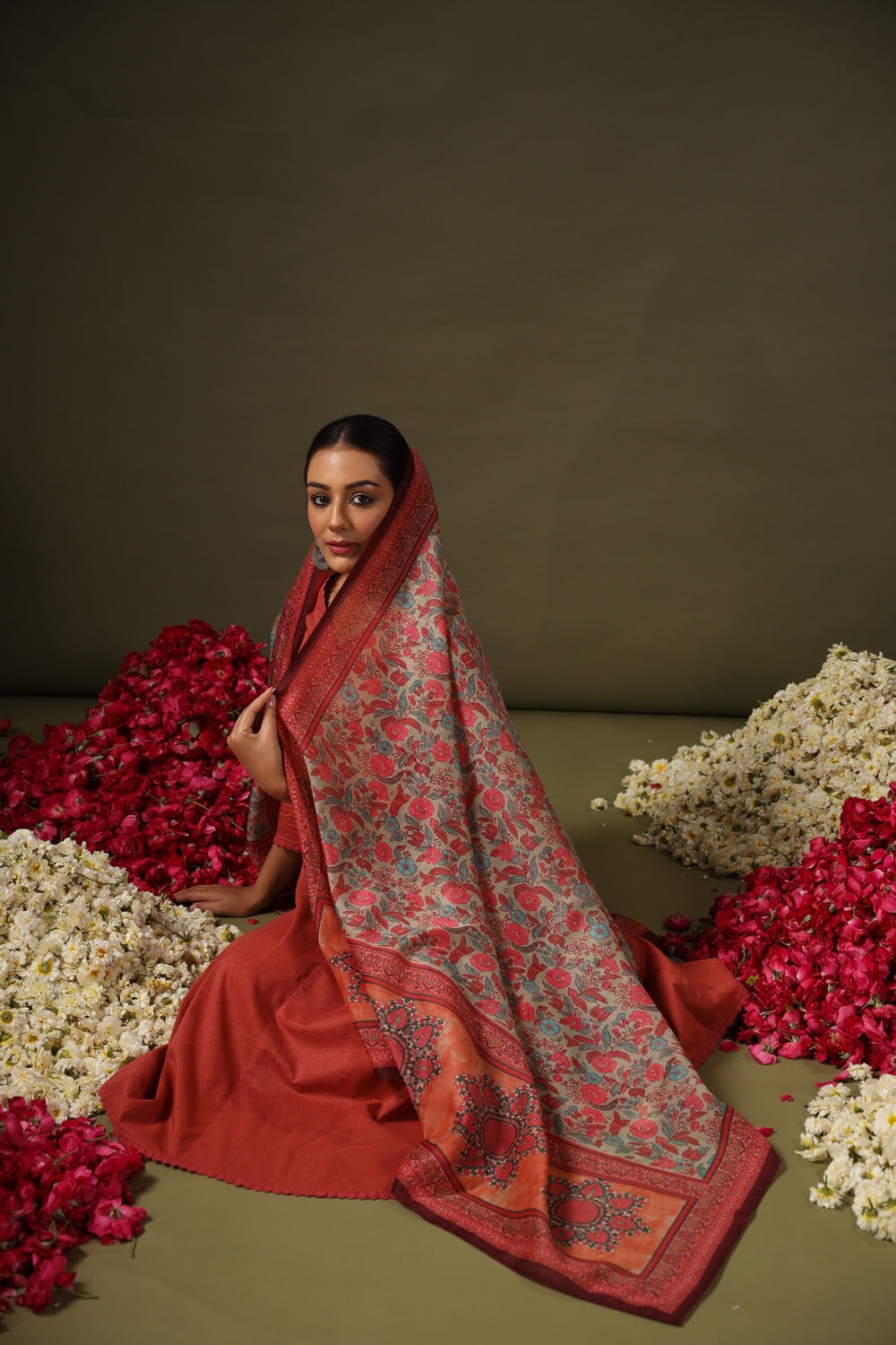 Woman draped in a red floral saree surrounded by flowers on a brown background
