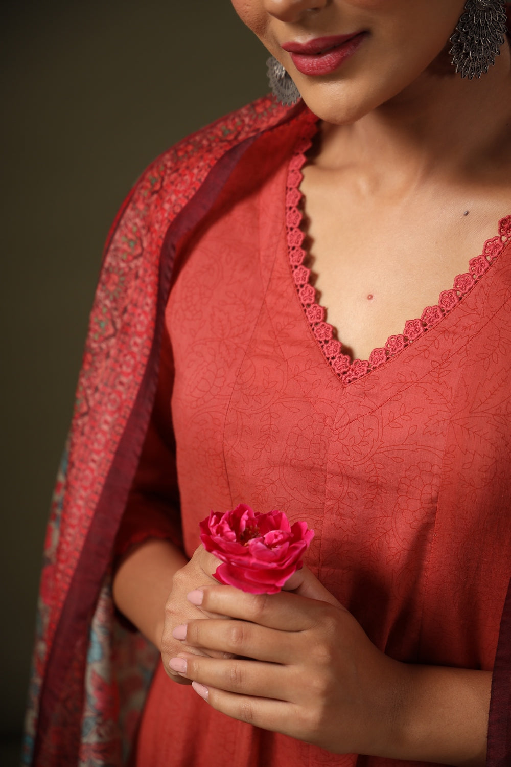 Woman wearing a red outfit with a floral accessory against a dark background