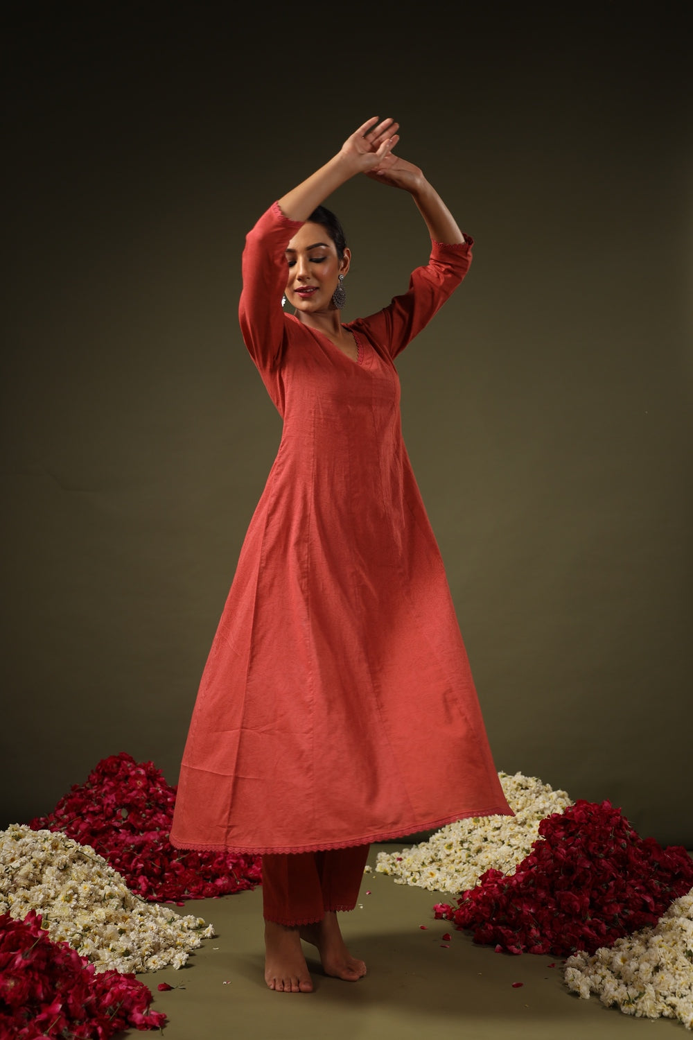 Woman in a red dress standing among flowers on a dark background