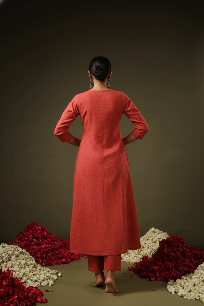 Person wearing a red kurta with white pants standing among red and white flowers on a dark background