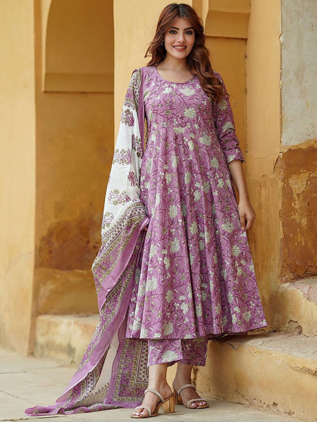 Woman wearing a pink floral outfit standing against a beige wall.