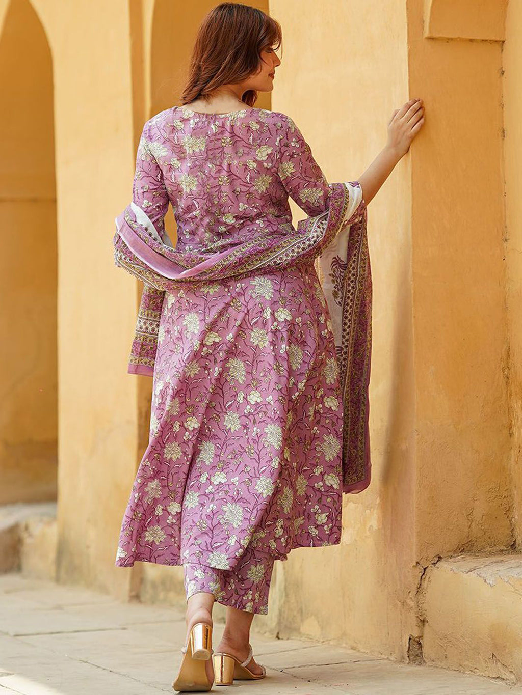 Woman in a pink floral dress standing against a beige wall.