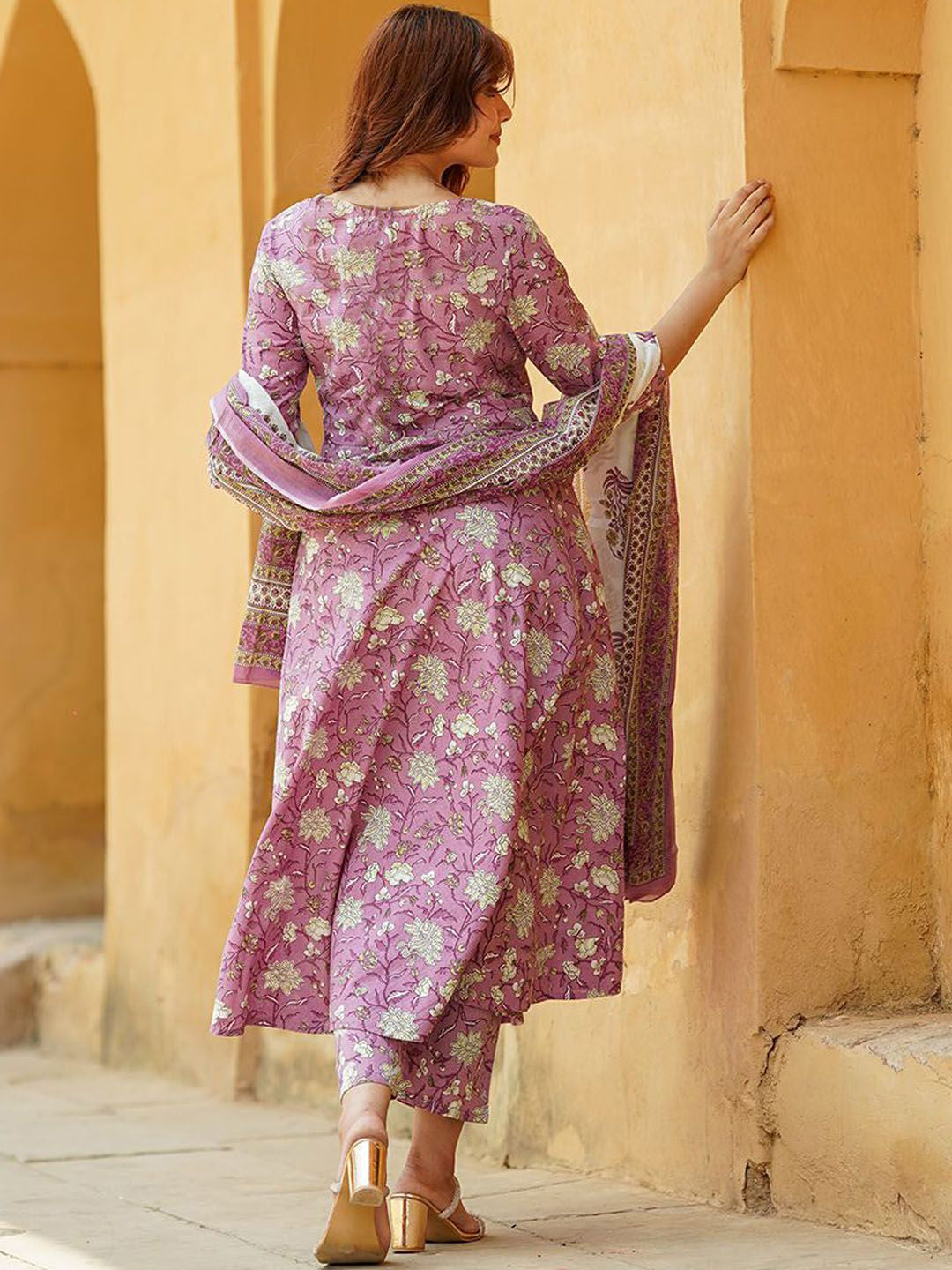 Woman in a pink floral dress standing against a beige wall.
