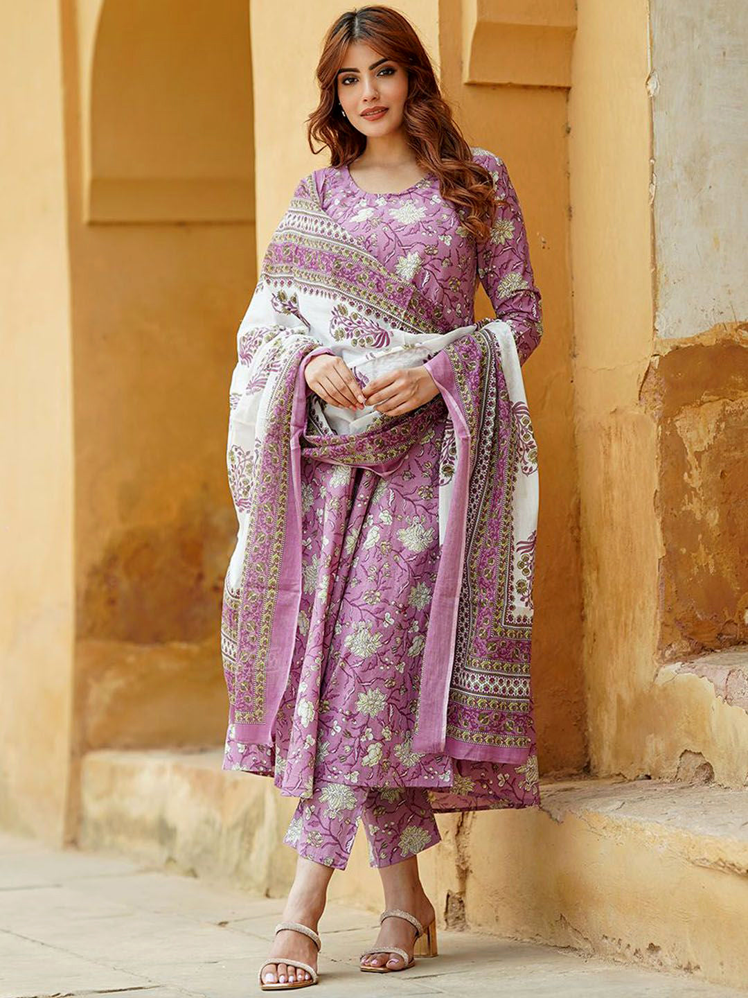 Woman wearing a purple and white traditional outfit standing against a beige wall.