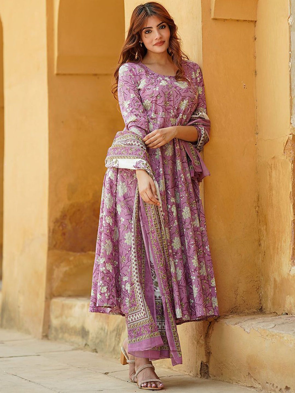 Woman wearing a purple floral dress standing against a beige wall.