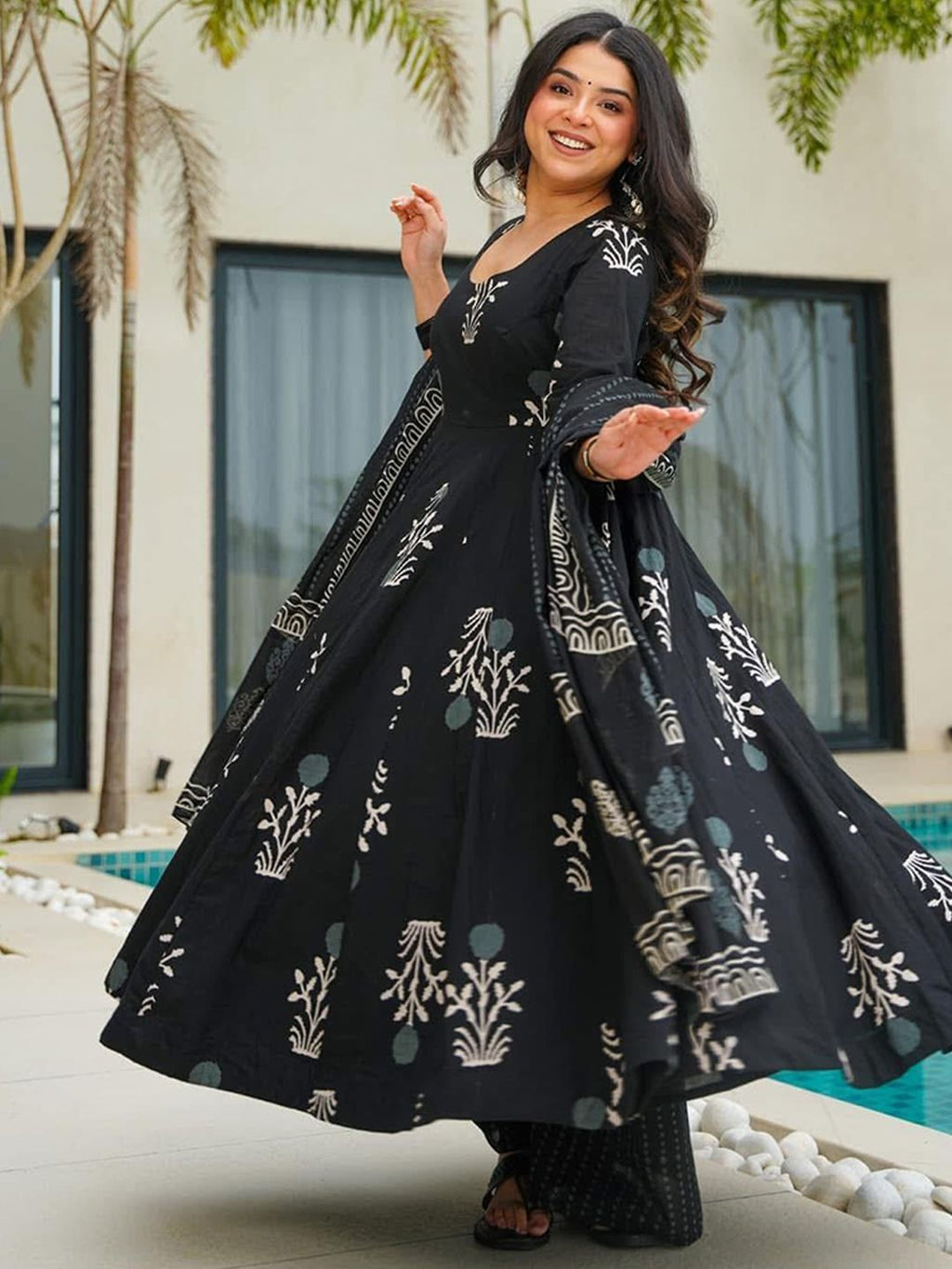 Woman in a black and white patterned dress standing outdoors near a pool.