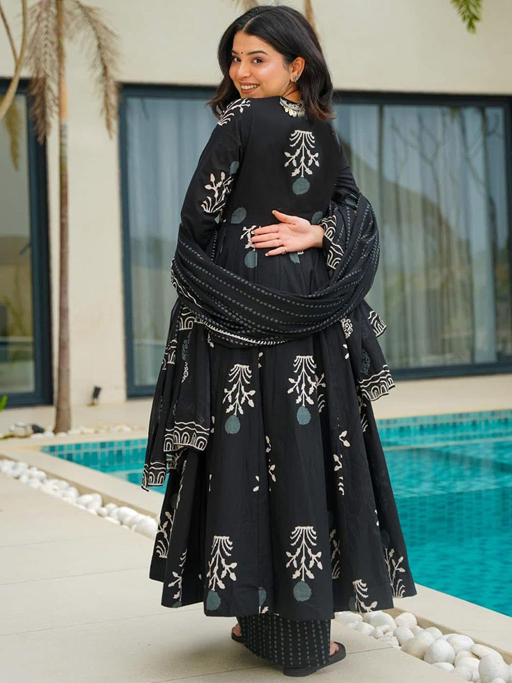 Woman in a black traditional outfit with white patterns standing by a pool.