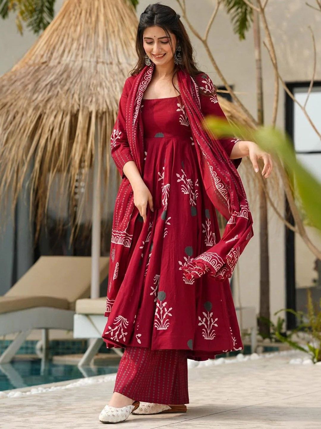 Woman in a red traditional outfit with white patterns standing by a poolside.