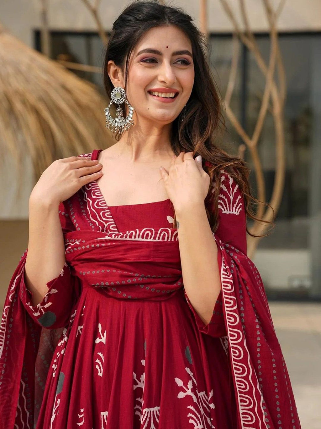 Woman wearing a red traditional outfit with white patterns, standing outdoors.
