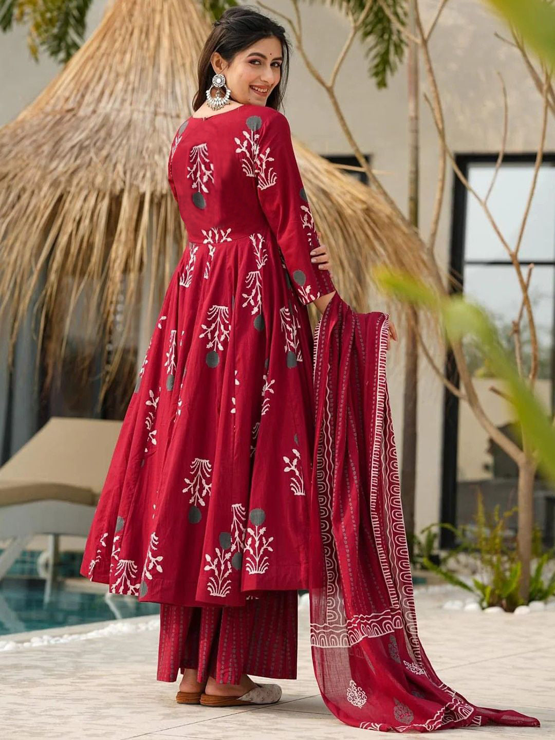 Woman wearing a red traditional outfit with white patterns in an outdoor setting.