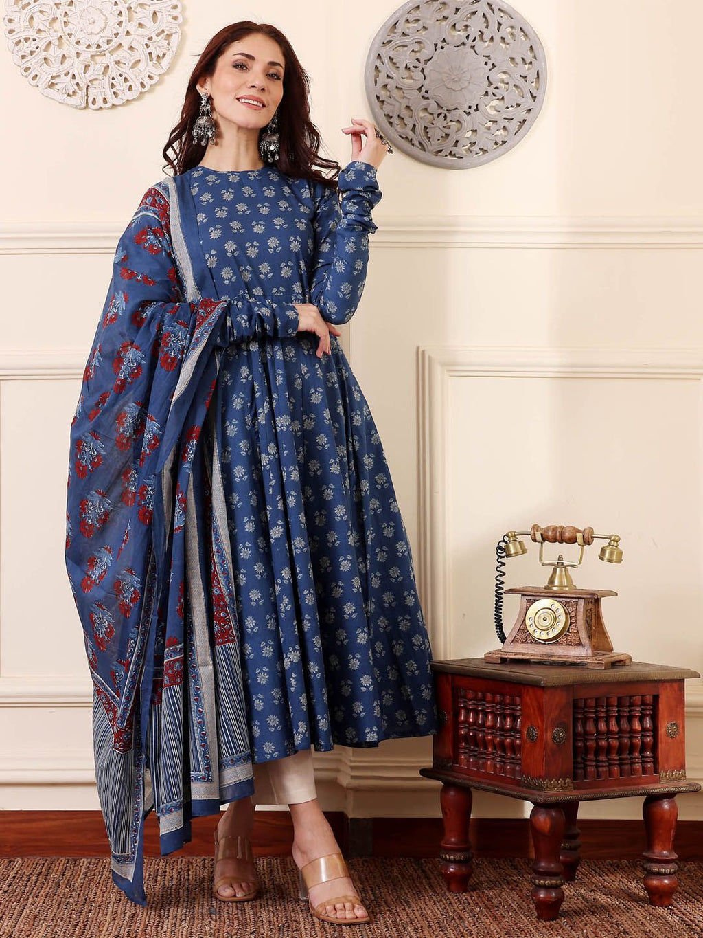 Woman in a blue floral dress with a matching shawl in a room with a vintage telephone and table.
