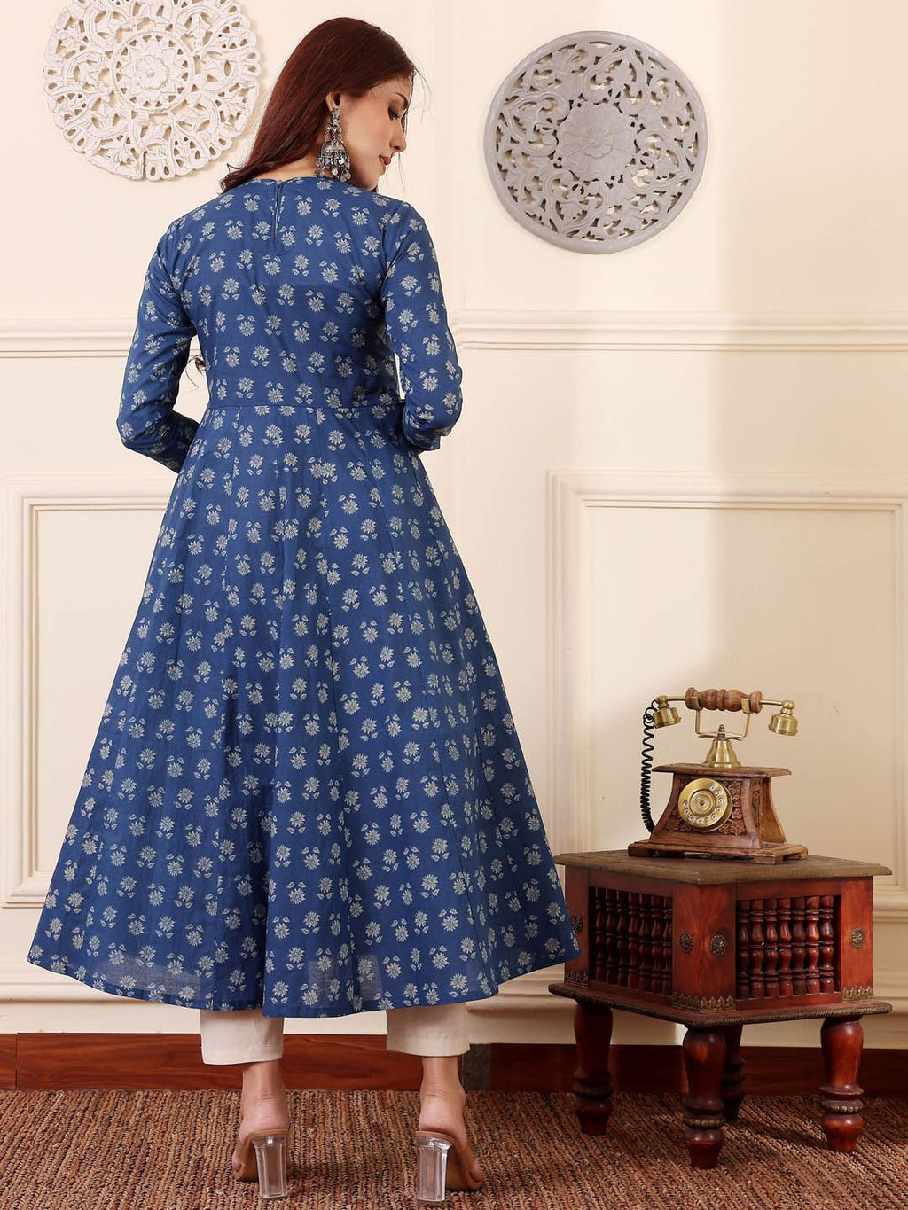 Woman wearing a blue floral dress in an elegant room with a vintage phone and table.