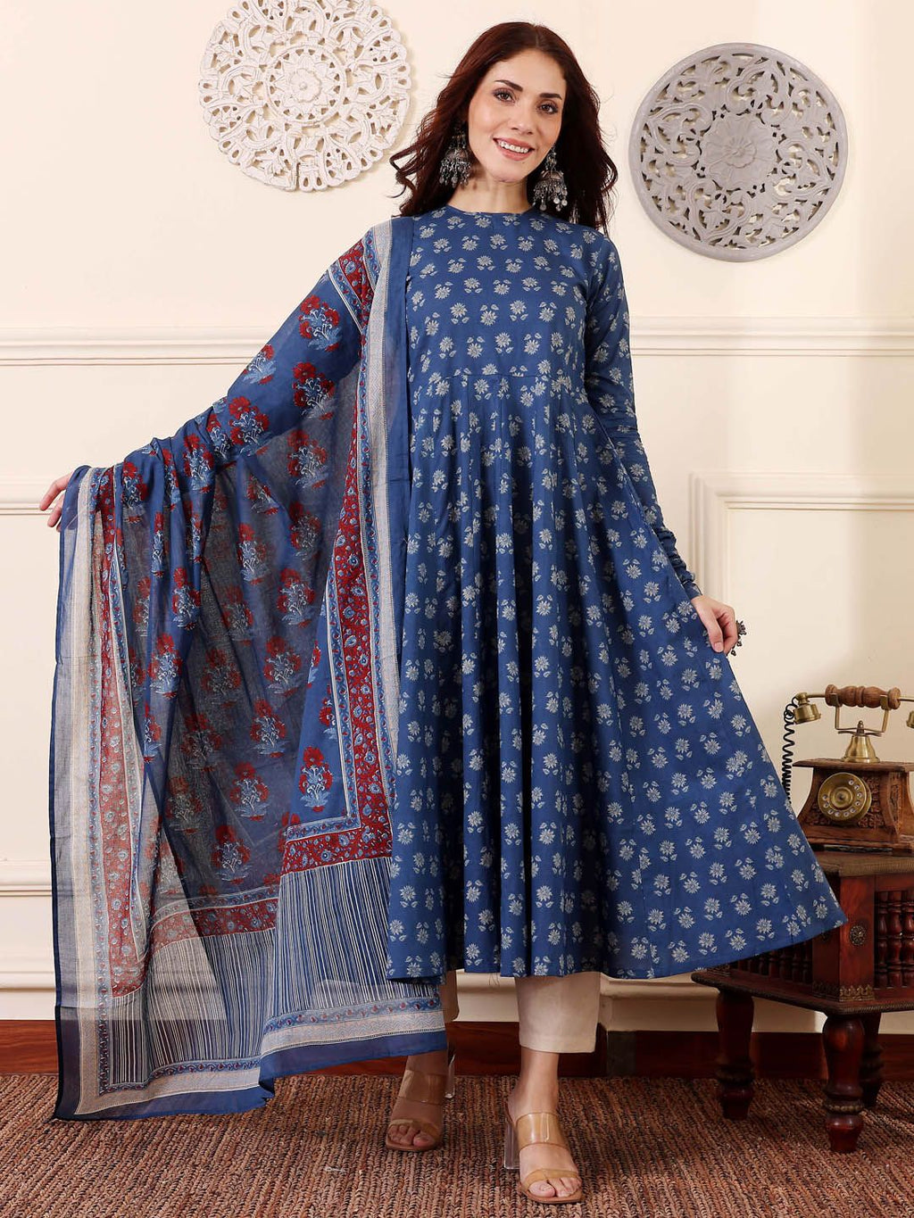 Woman wearing a blue traditional outfit with a matching dupatta in a decorated room.