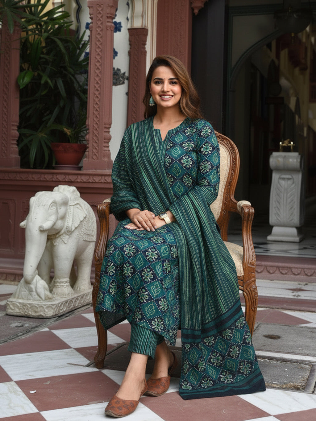 Woman in a green traditional outfit sitting on a chair in an ornate indoor setting.