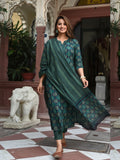 Woman in a green traditional outfit standing in an ornate indoor setting with decorative elements.