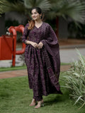 Woman in a purple patterned outfit standing outdoors with greenery in the background