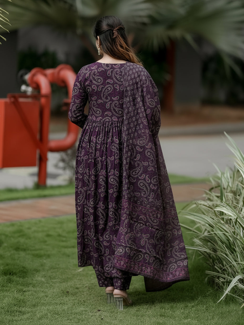 Woman in a long purple patterned dress standing on grass with blurred background