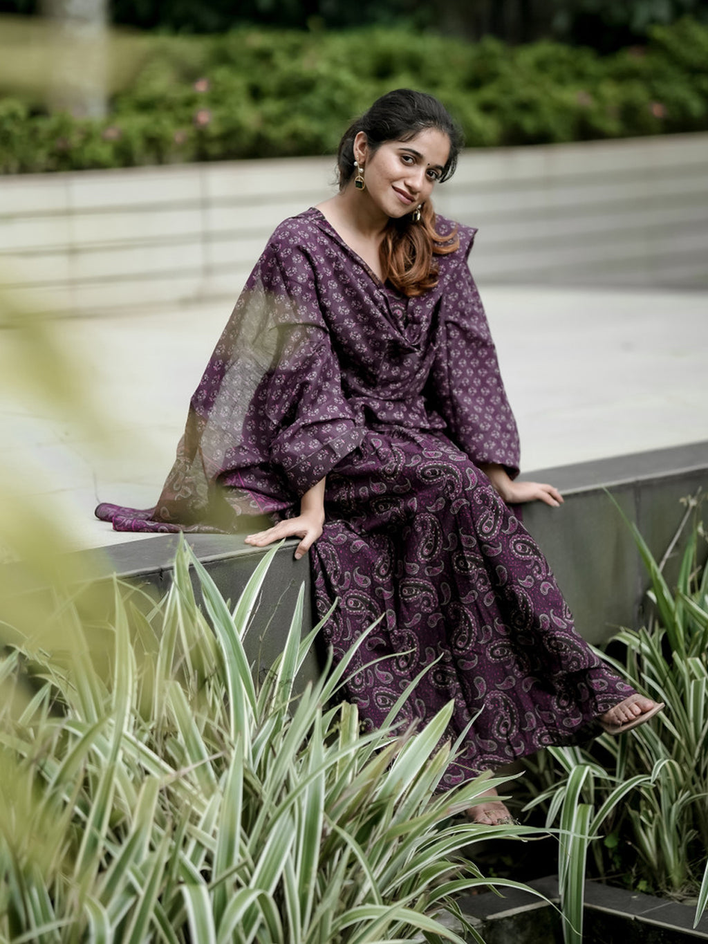 Woman in a purple patterned dress sitting outdoors with greenery around