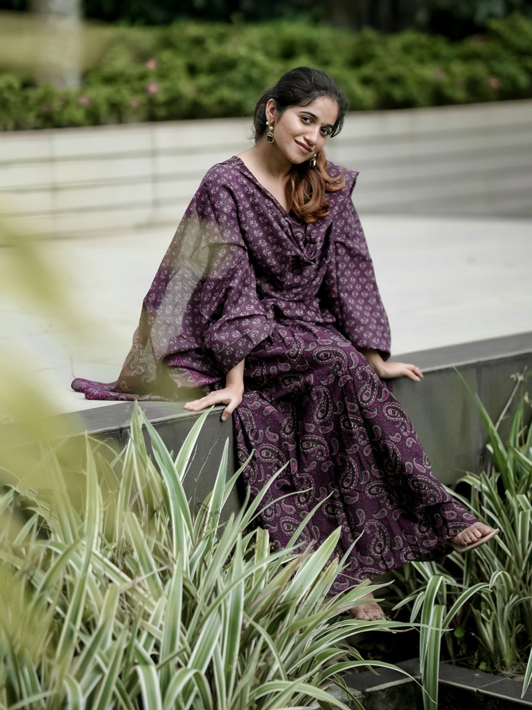 Woman in a purple patterned dress sitting outdoors with greenery around