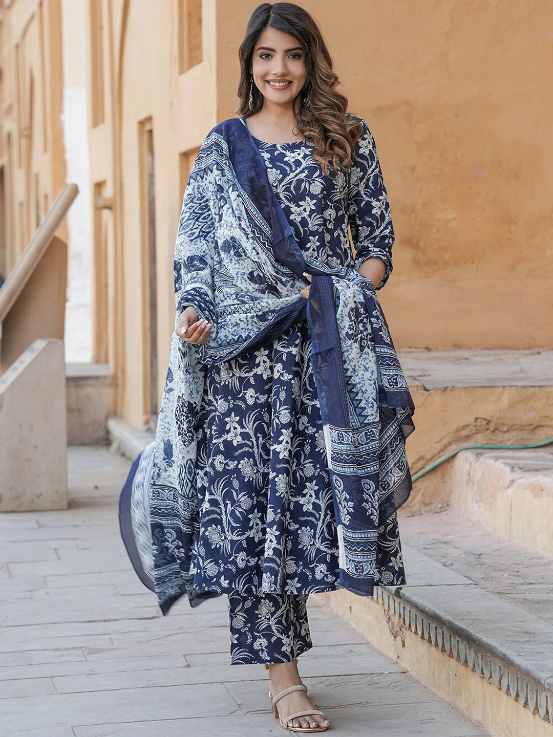 Woman wearing a blue floral traditional outfit standing in front of a beige wall.