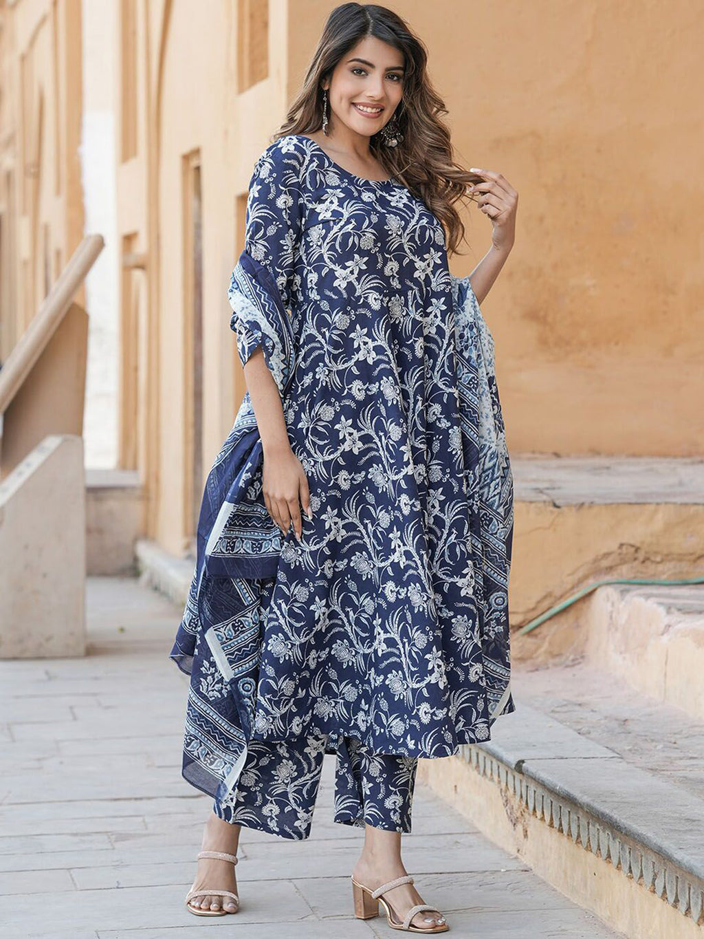 Woman wearing a blue floral dress standing in front of a beige wall.