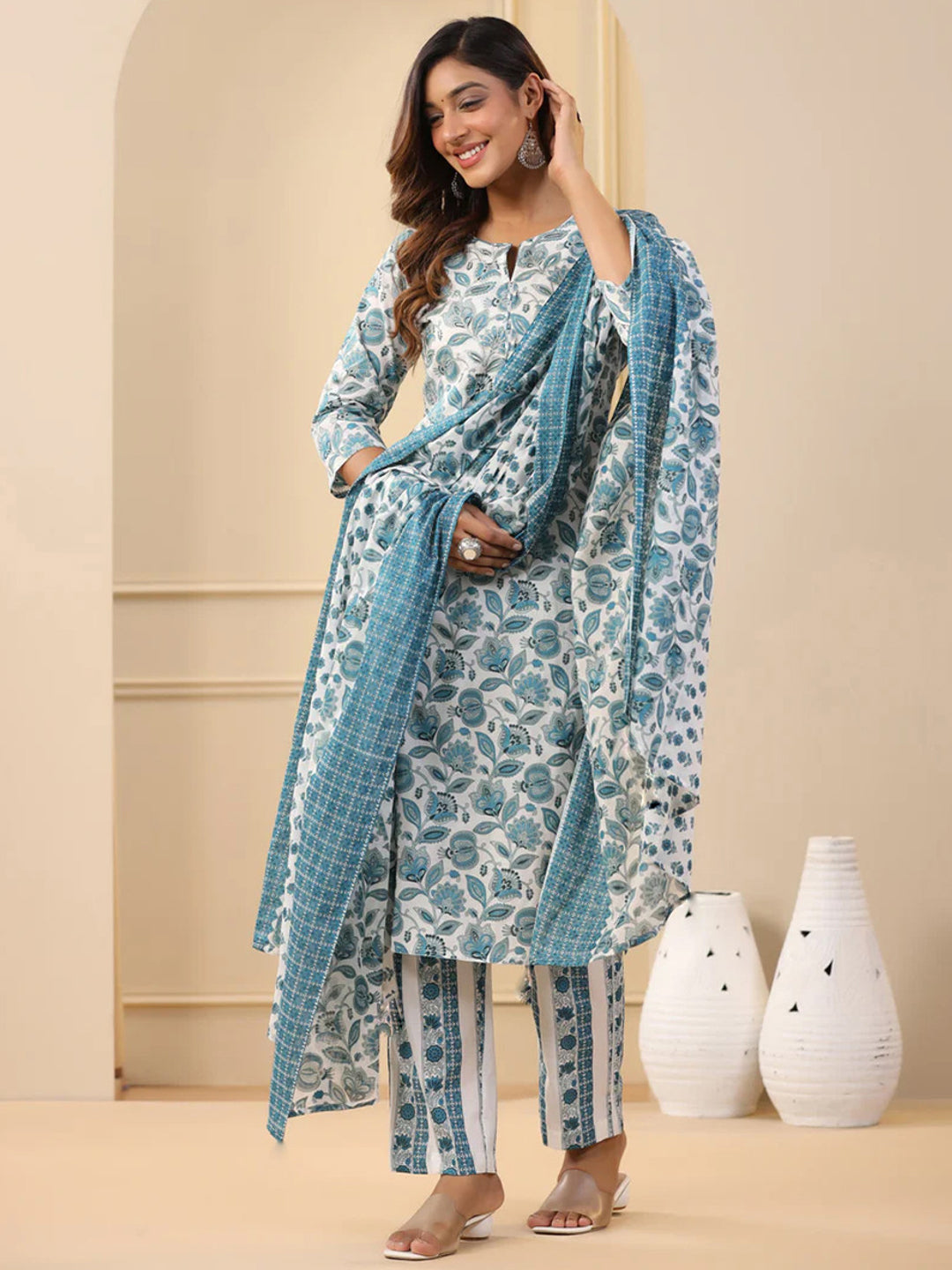 Woman wearing a blue and white floral outfit with a matching dupatta in a minimalistic setting.