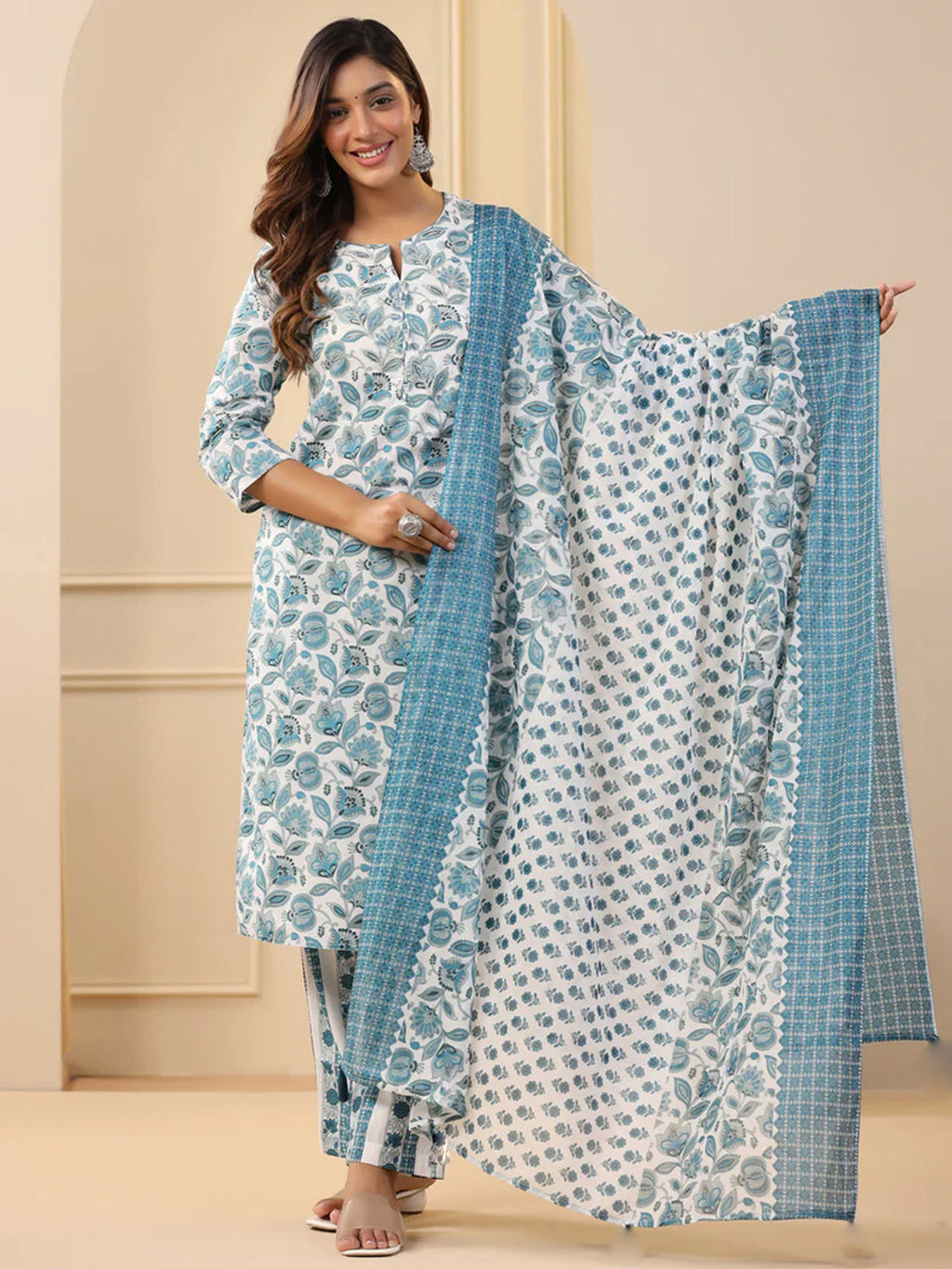 Woman wearing a floral kurta with matching pants and a blue dupatta against a beige background