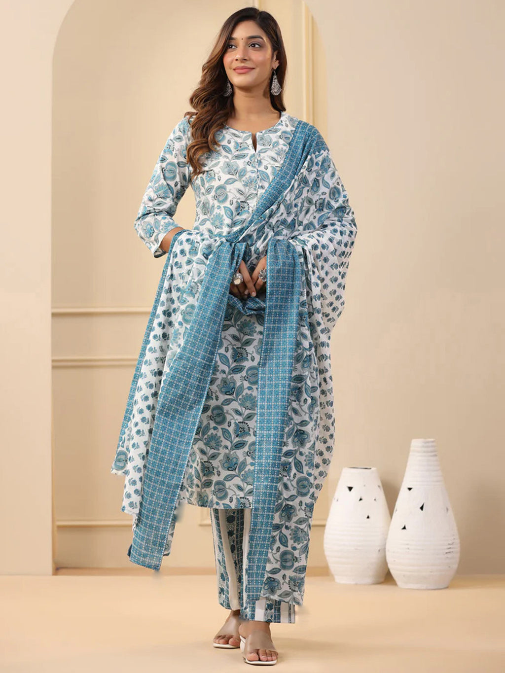 Woman wearing a blue and white floral outfit with a matching dupatta in a minimalistic setting.