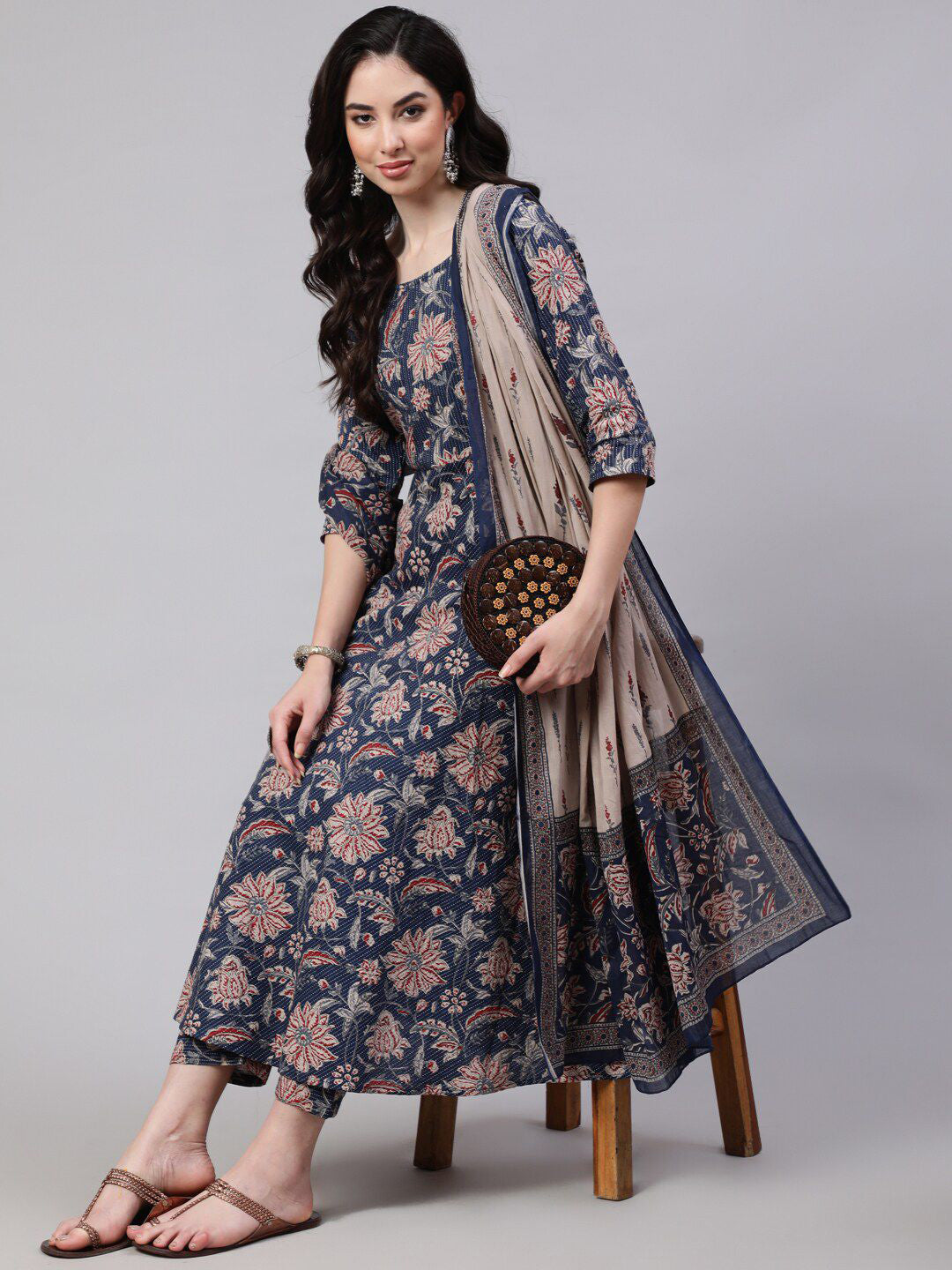 Woman wearing a floral dress with a scarf, standing on a stool against a gray background