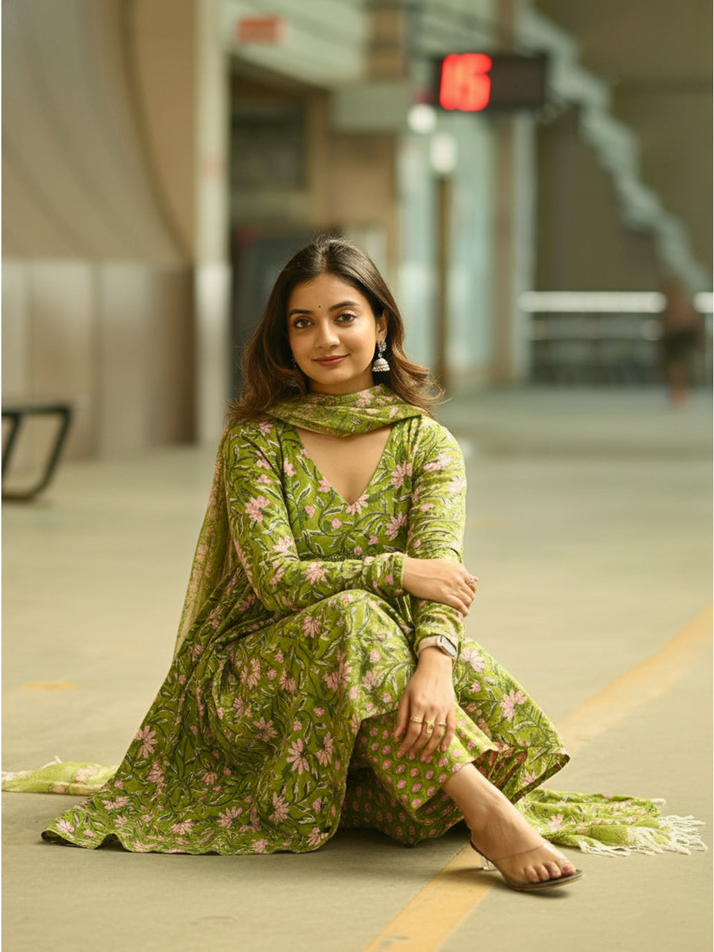 Woman in a green floral outfit sitting on the floor in an indoor setting