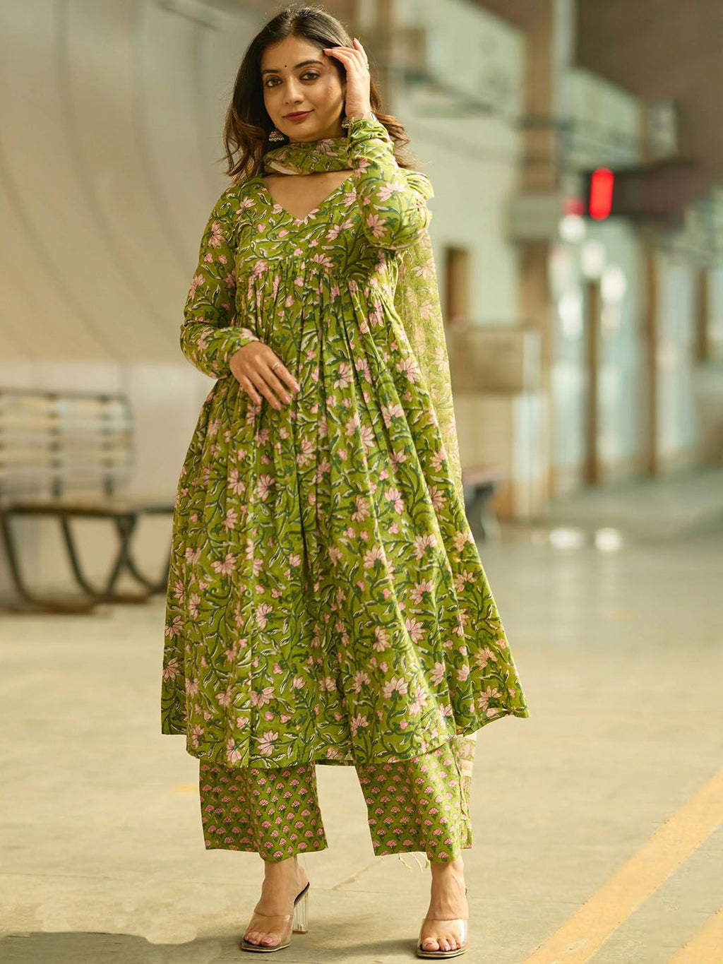 Woman wearing a green floral outfit standing on a street.