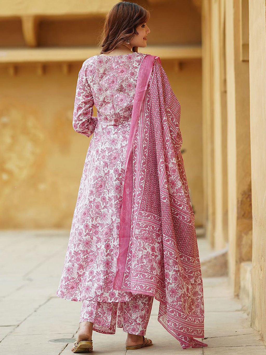 Woman in a pink and white traditional outfit with a matching dupatta standing in front of a beige wall.