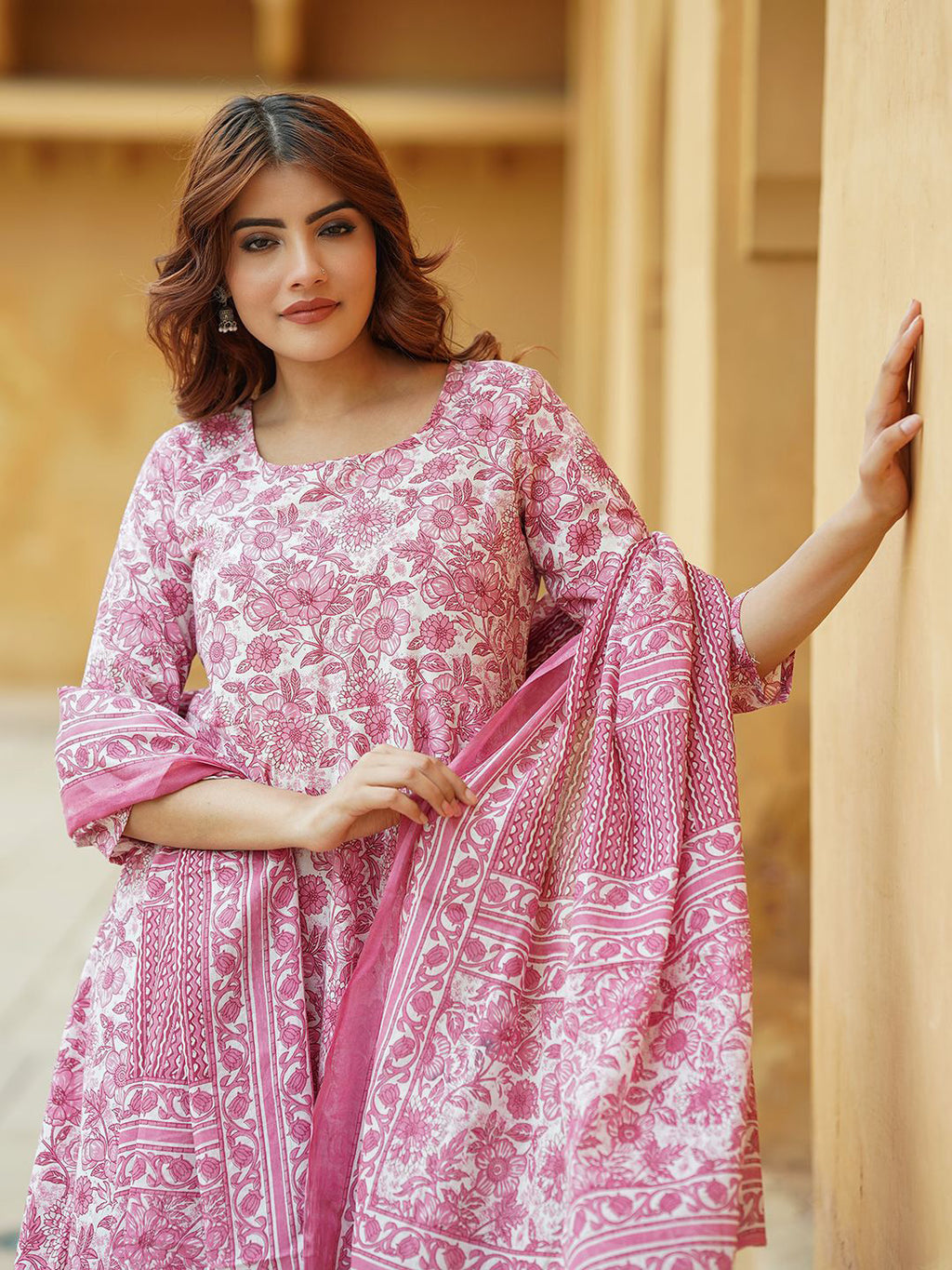 Woman wearing a pink and white patterned outfit against a beige wall.