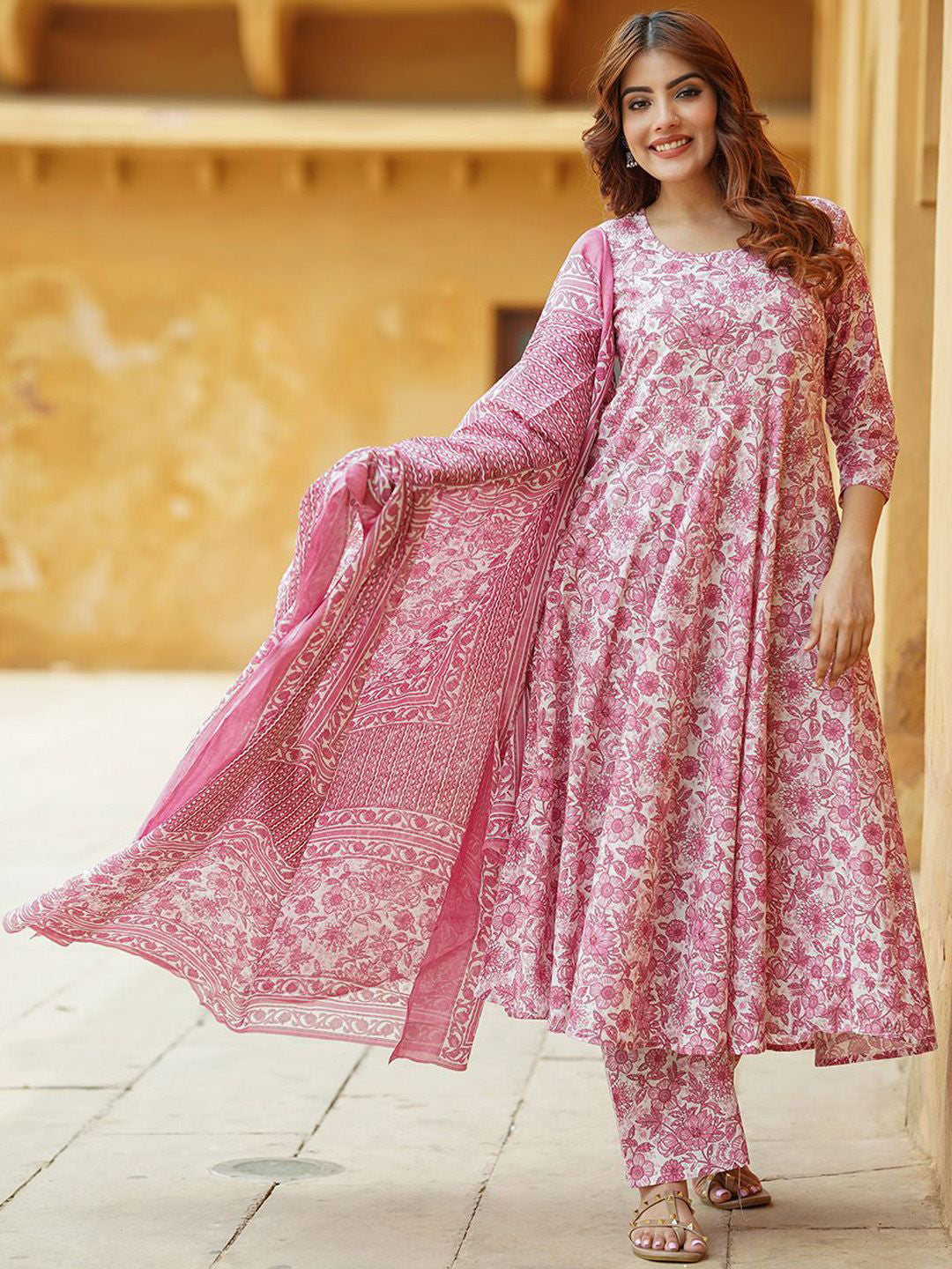 Woman wearing a pink floral outfit standing in front of a warm-toned wall.