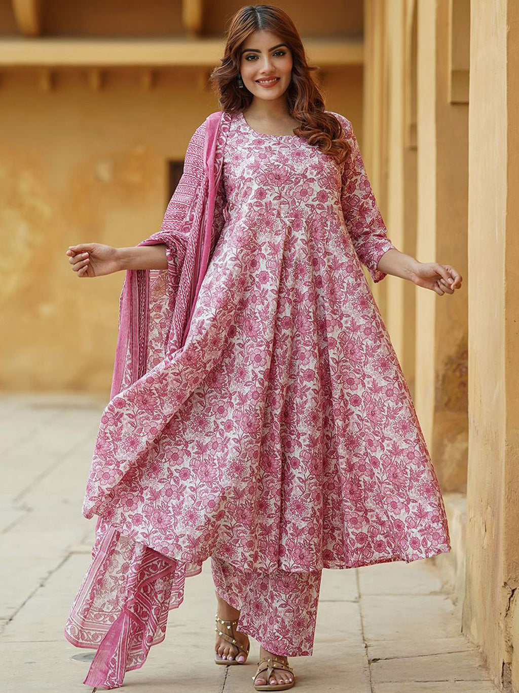 Woman wearing a pink floral traditional outfit with a dupatta in an outdoor setting.
