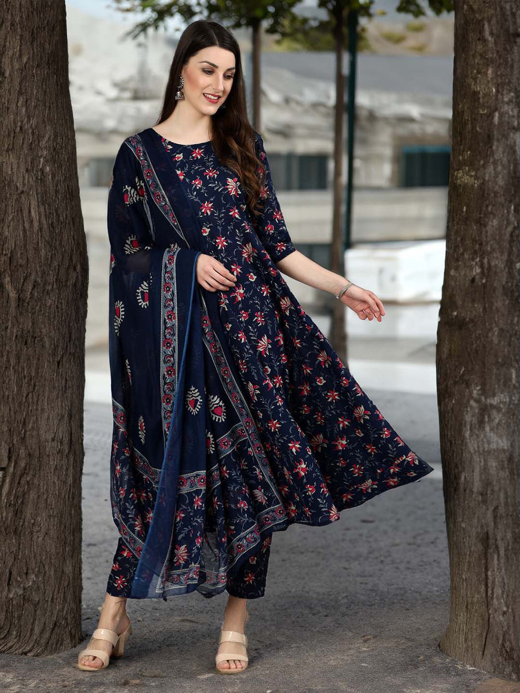 Woman wearing a navy blue floral dress standing between two trees.