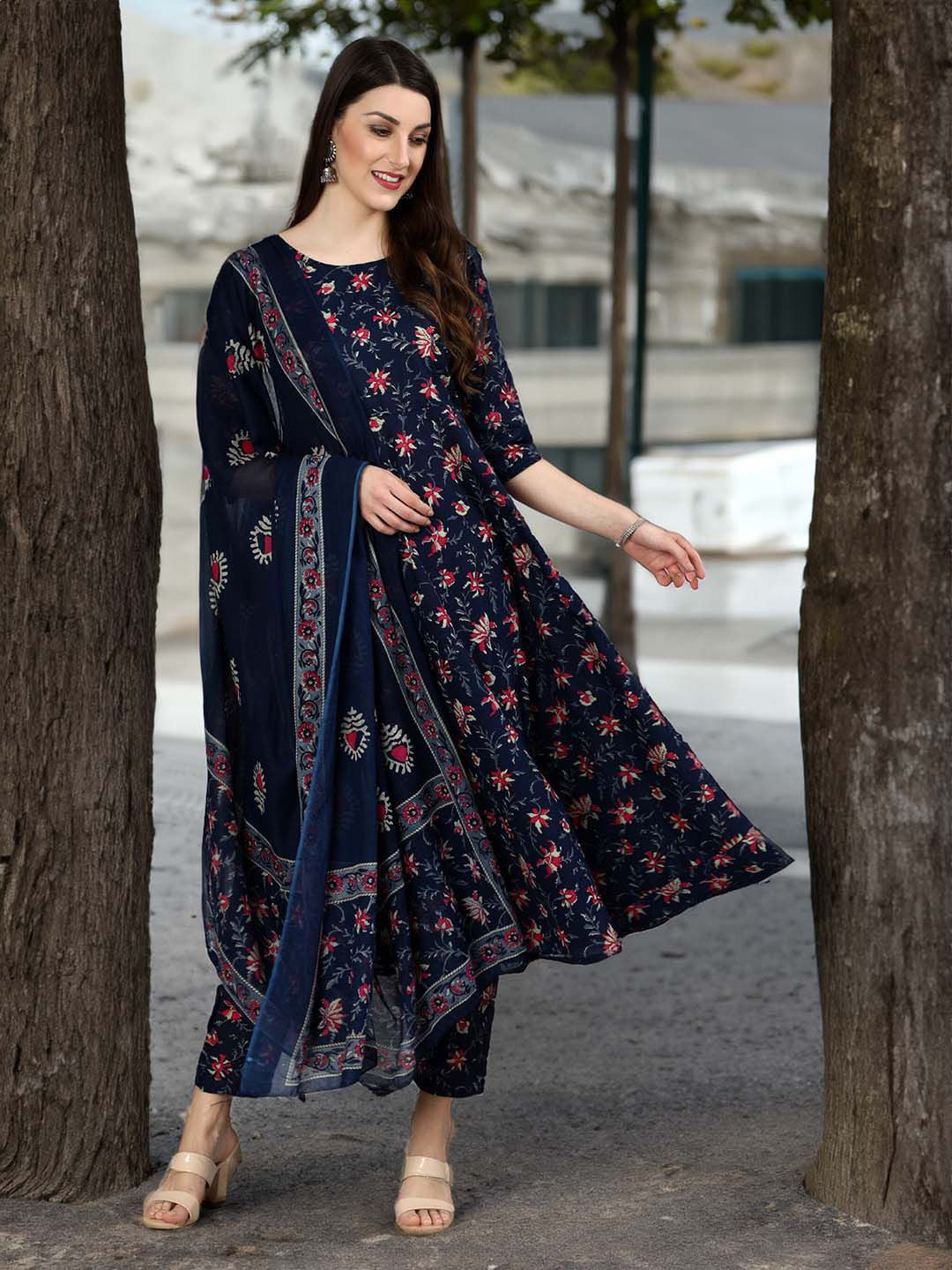 Woman wearing a navy blue floral dress standing between two trees.