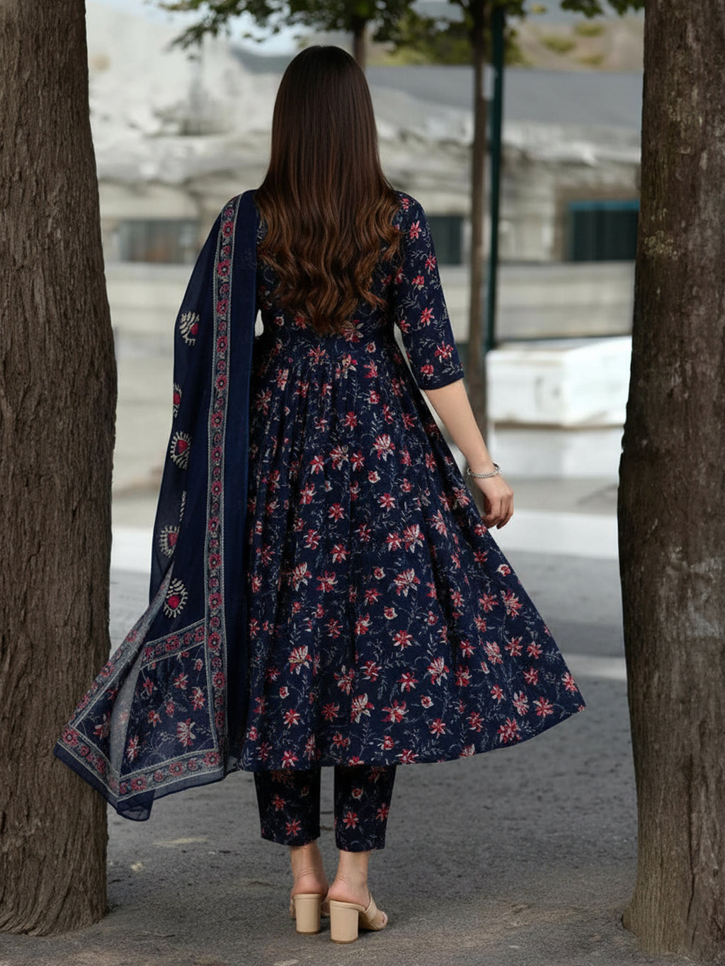 Woman in a navy floral dress with a matching dupatta walking between trees.