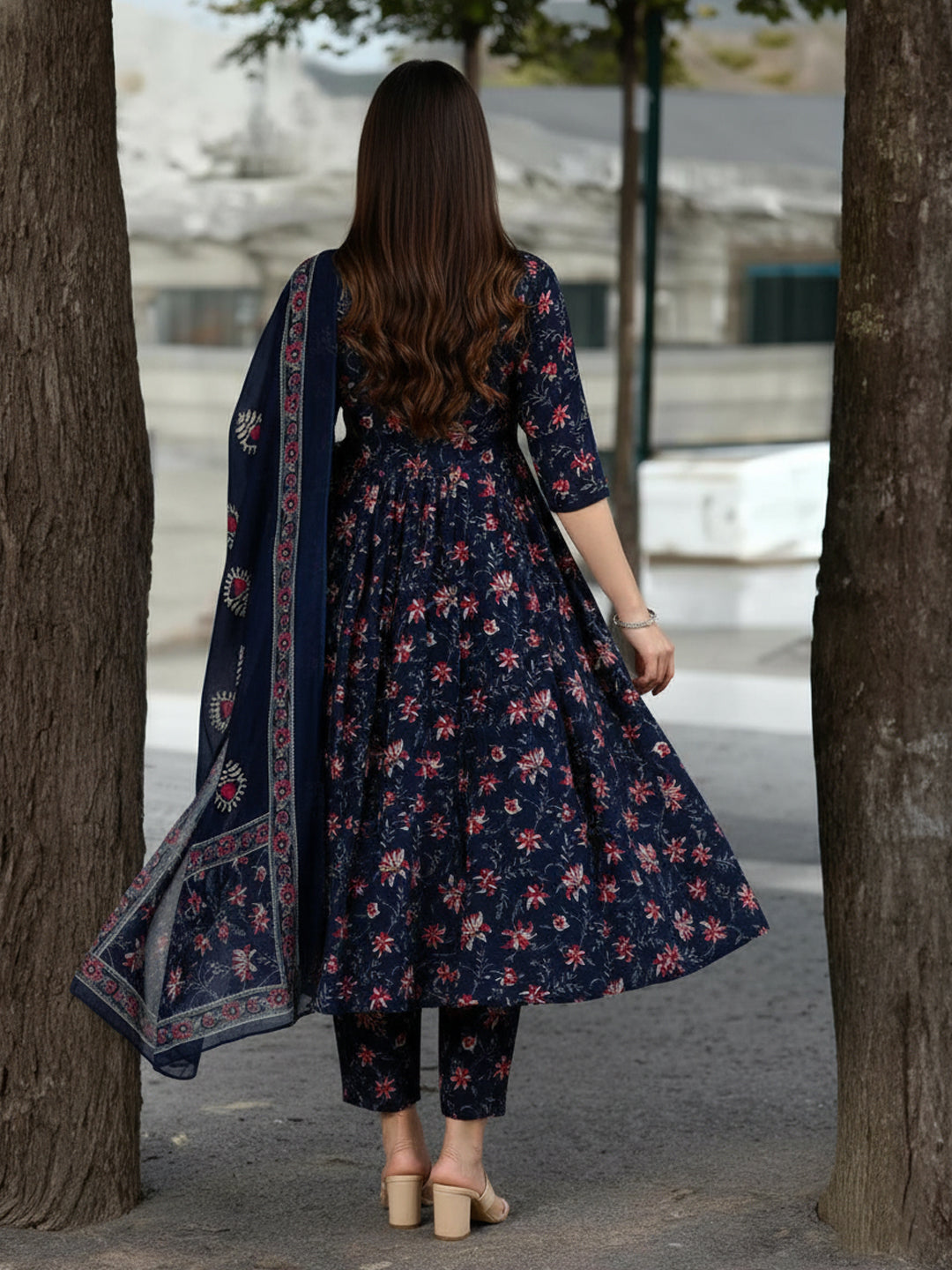 Woman in a navy floral dress with a matching dupatta walking between trees.