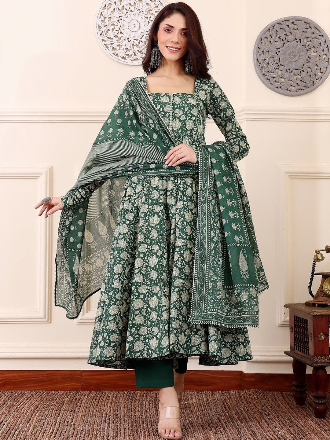 Woman wearing a green traditional outfit with a matching shawl in a decorative room.