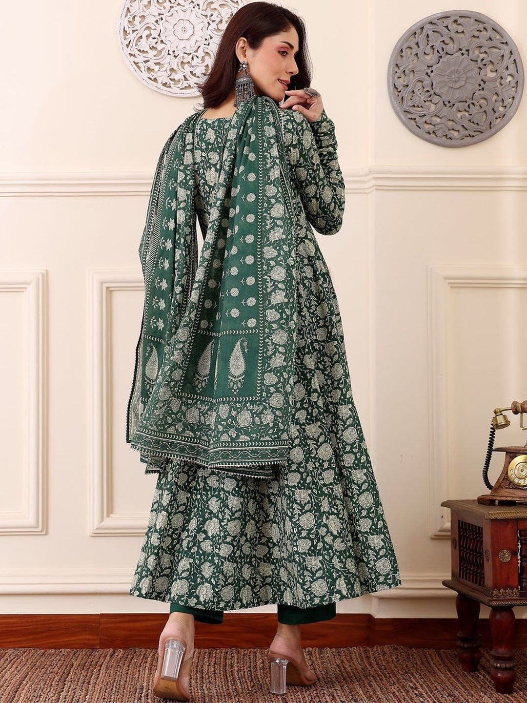 Woman wearing a green floral traditional outfit in a decorated room.