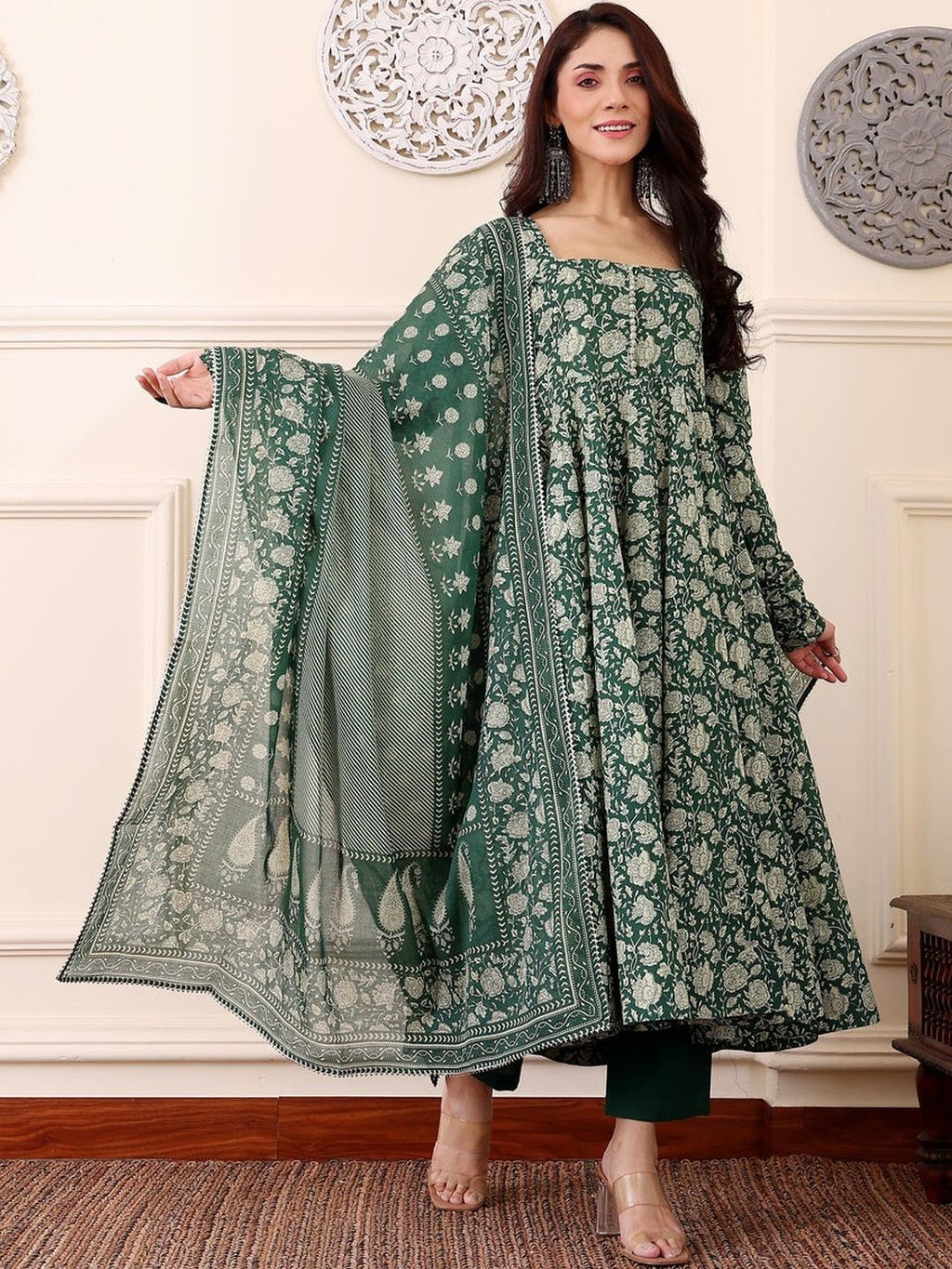 Woman wearing a green traditional outfit with a matching dupatta in an elegant room.